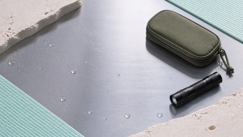 Water droplets on satin steel with an EDC pouch and compact flashlight