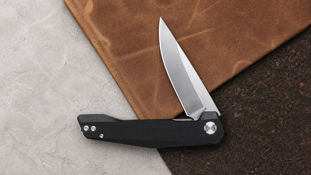 Open black HOPIAN Vex knife across stone, canvas, and cork surfaces