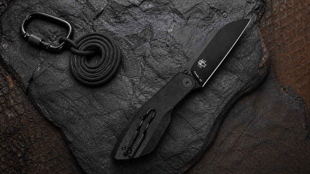 Open black HOPIAN Periodic knife with a carabiner and cord on rugged surfaces