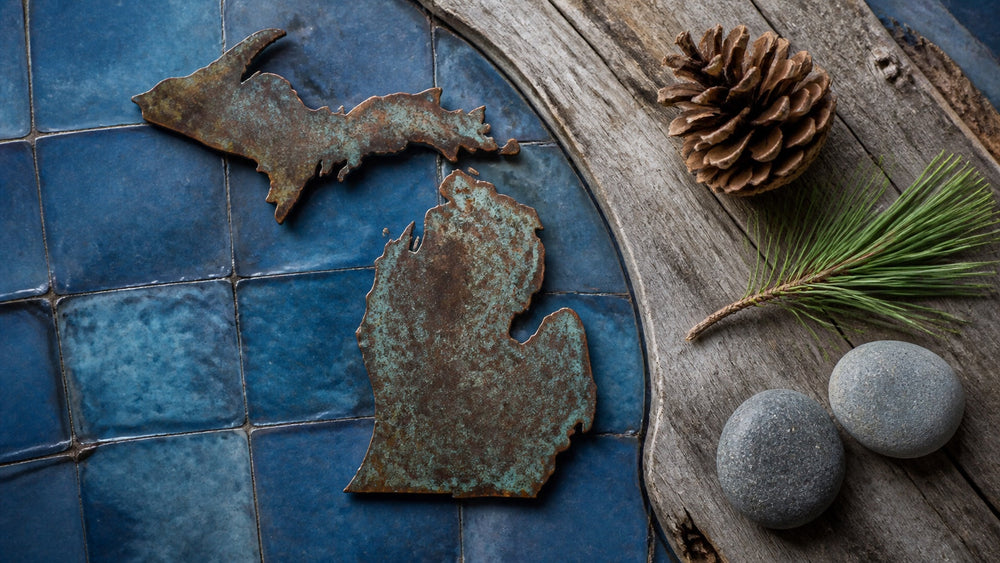 Overhead Michigan silhouette with a pine cone, pine sprig, and lake stones