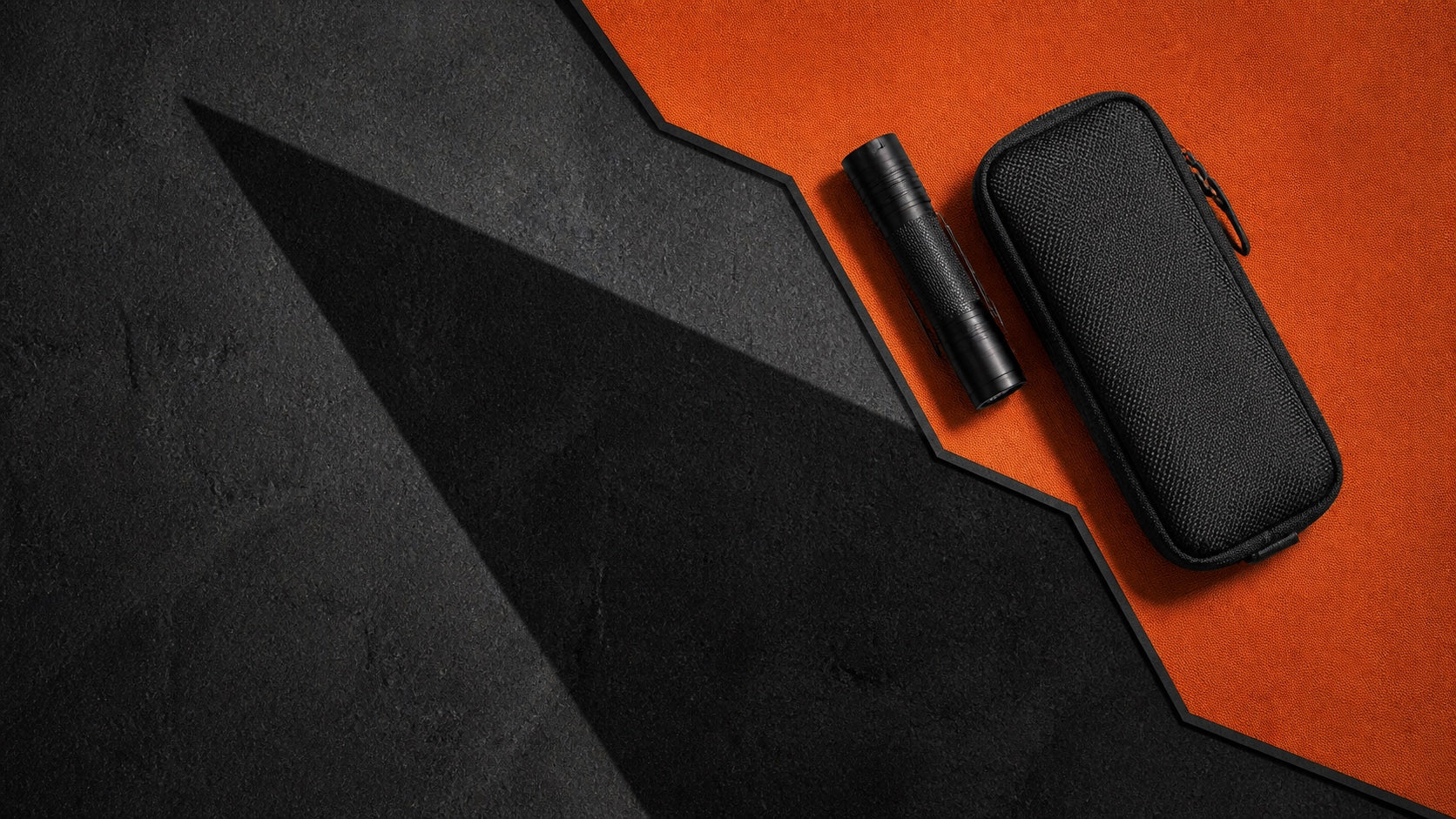 Angular black and orange EDC scene with a flashlight and compact pouch